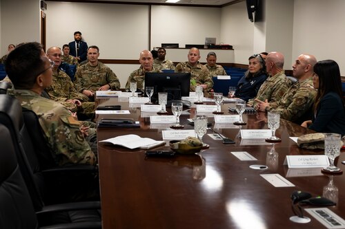 A group of military members sit around a conference room table.