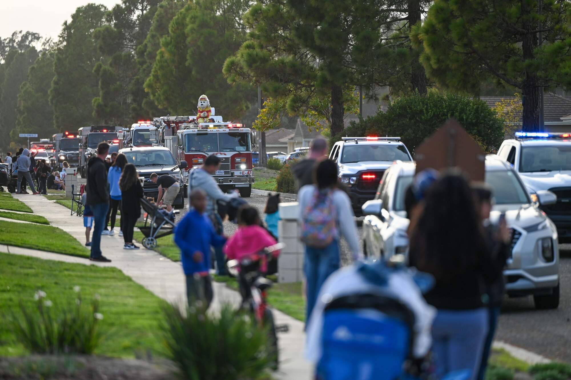 People gather on a sidewalk to watch the fire parade coming down the street.