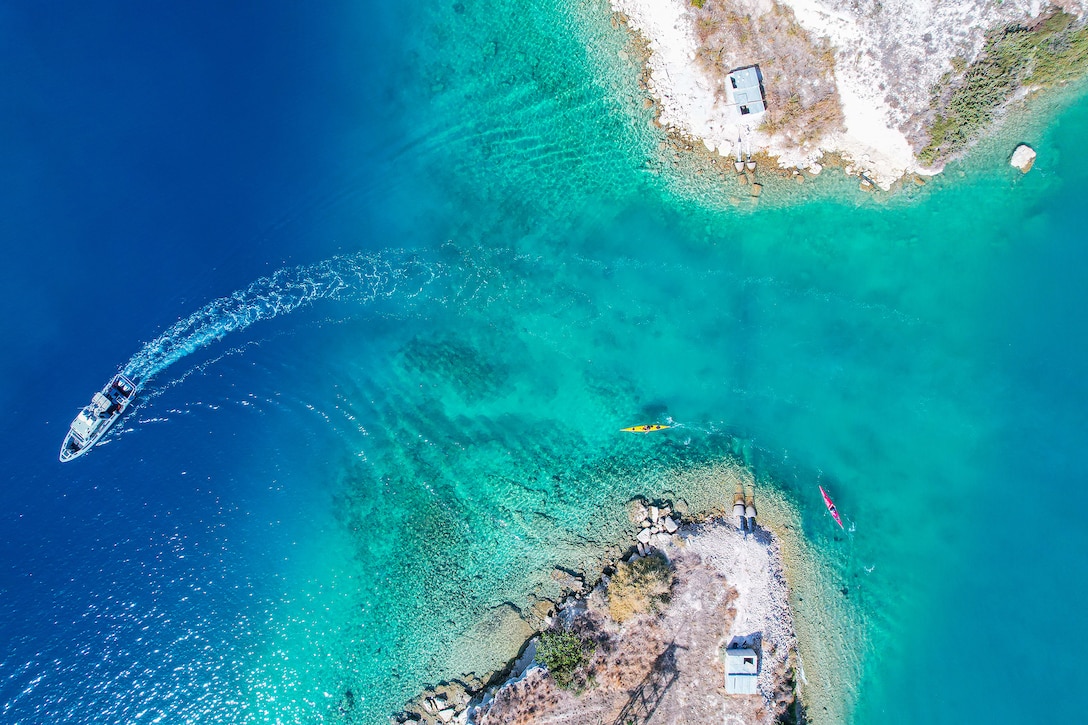 Aerial view of a boat sailing in blue water away from a peninsula during daylight.