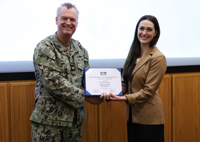 Naval Surface Warfare Center, Philadelphia Division (NSWCPD) Commanding Officer Capt. Joseph Darcy presents a letter of appreciation to Sarah Tuberty during the National Disability Employment Awareness Month Observance held at the command on Oct. 2, 2024. The observance featured a special presentation by Nicole Kelly Marti and Tuberty, hosts of the podcast “Disarming Disability.” (U.S. Navy Photo by Phil Scaringi, ctr)