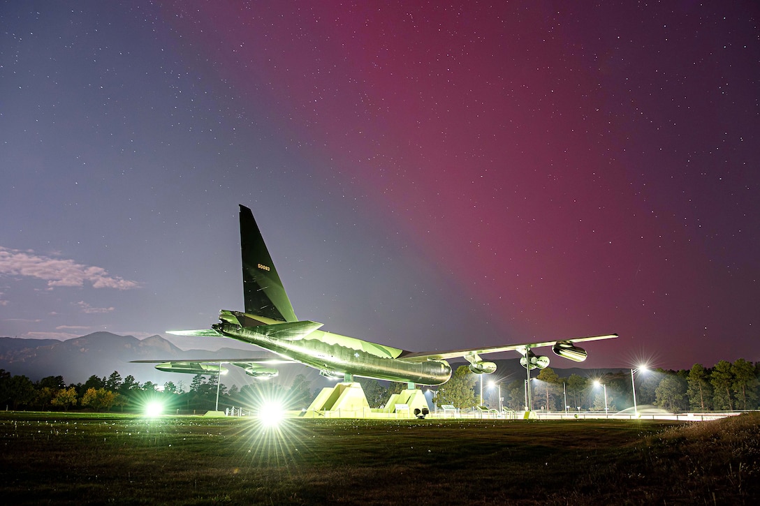 Spotlight shine on an aircraft statue under a starry night sky with a pinkish hue.