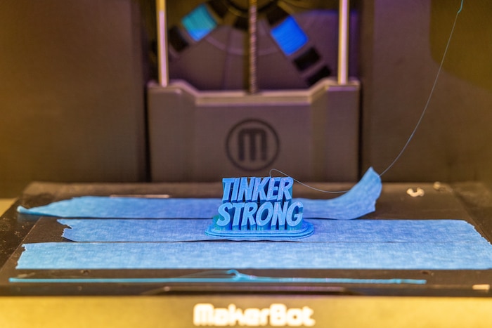A picture of the Tinker Library 3D printer printing out the words "Tinker Strong".