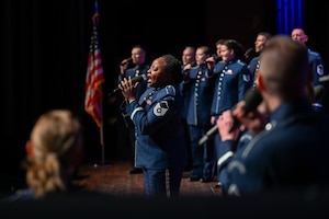 Photo of Singing Sergeants in which one performer is performing a solo. All Singing Sergeants are holding a microphone on stage.