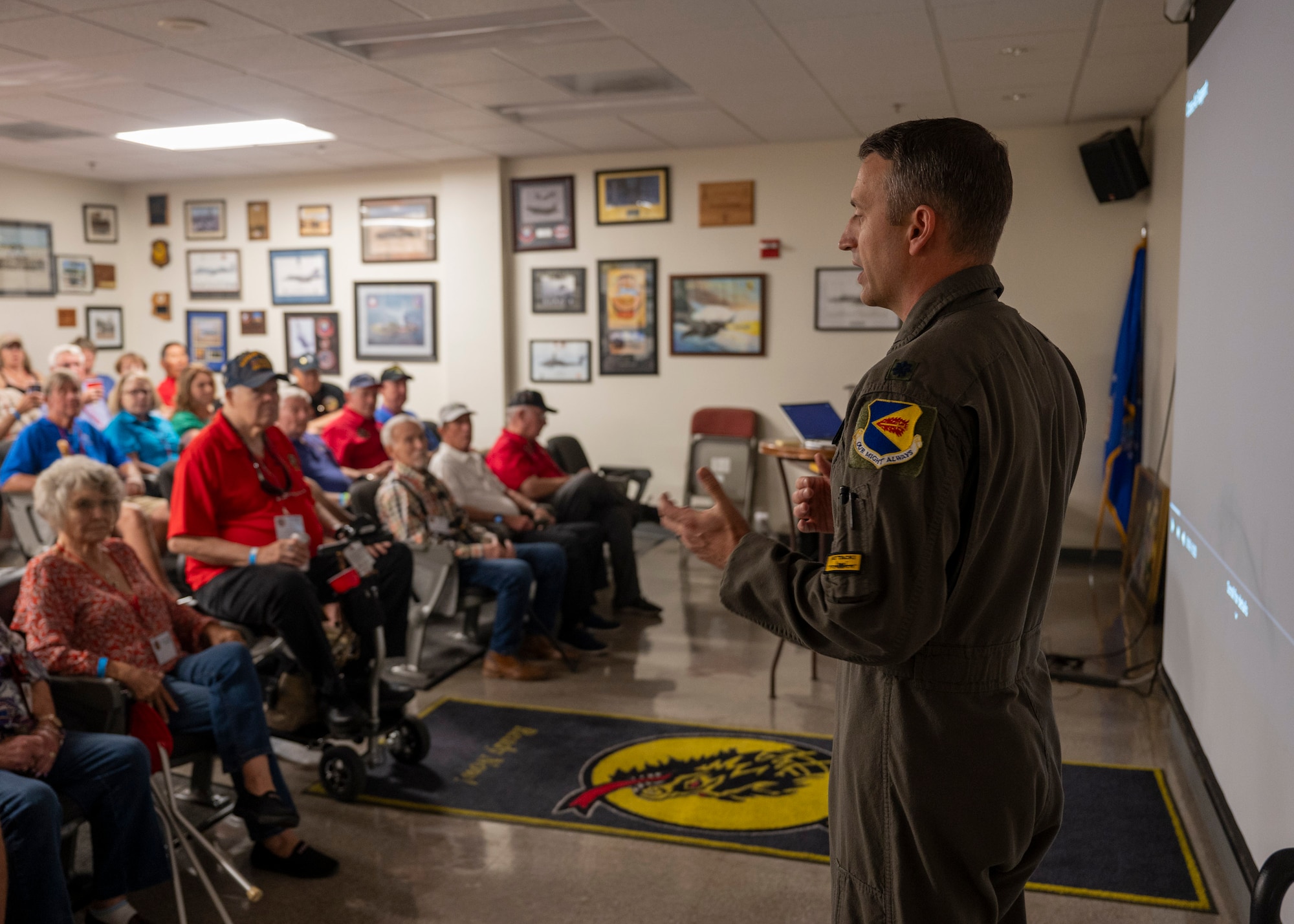 A man in a military flight suit speaks to a crowd of retied people.