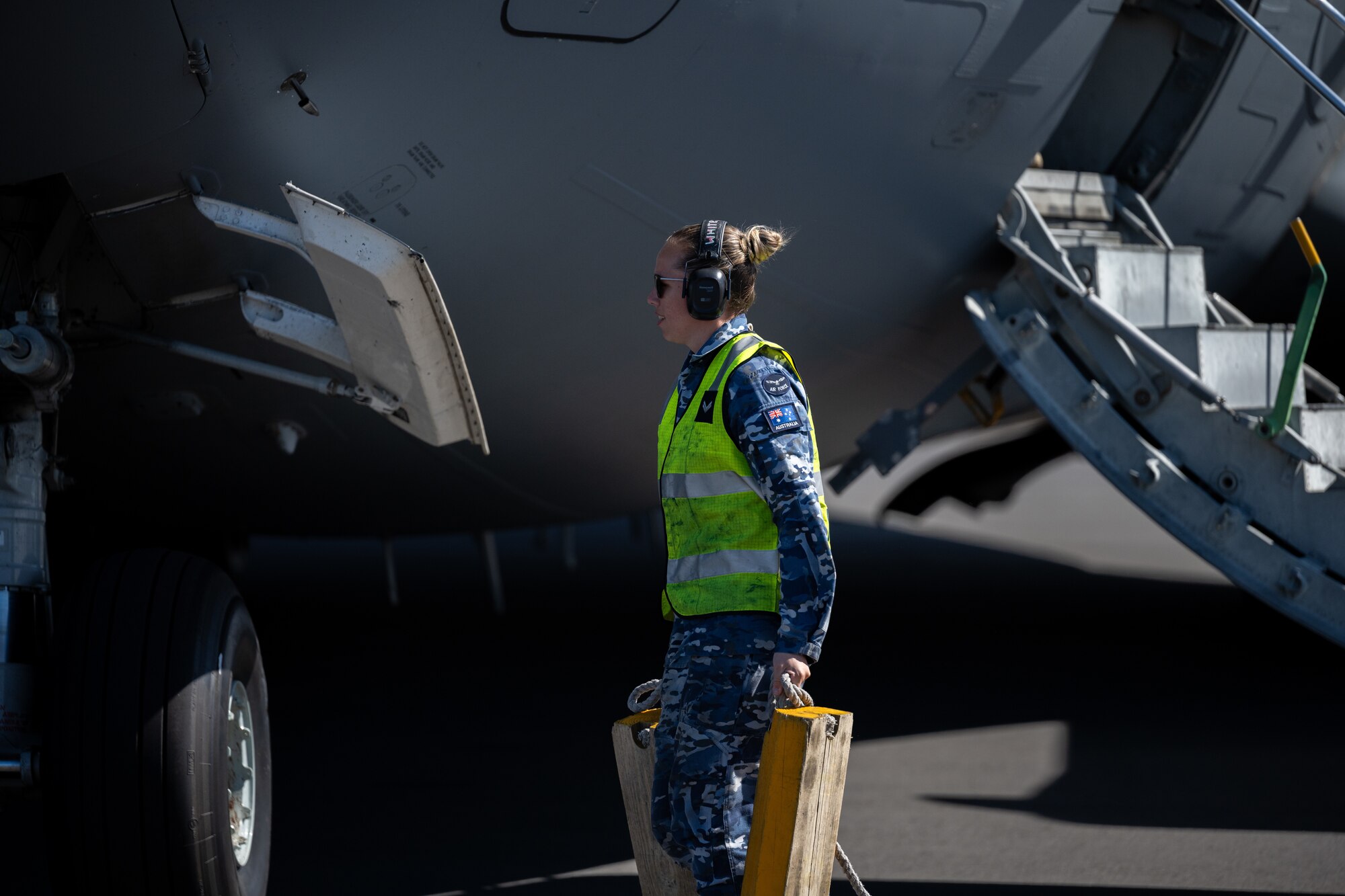 Royal Australian Air Force Airman carries two large yellow aircraft chalks in front of a C-17 Globemaster III.