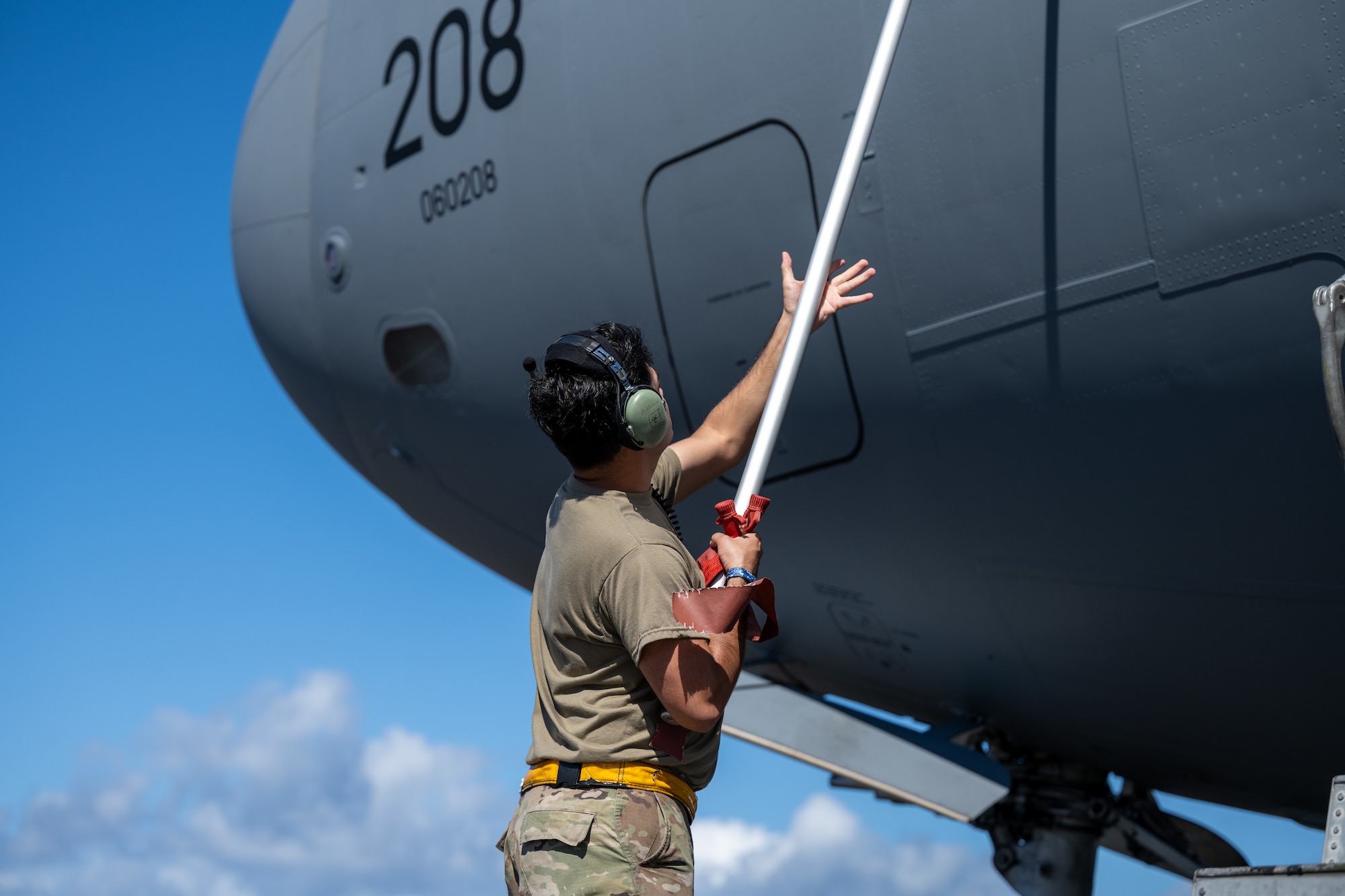 U.S. Airmen pulls a tag off a C-17 Globemaster III, using a long pole.