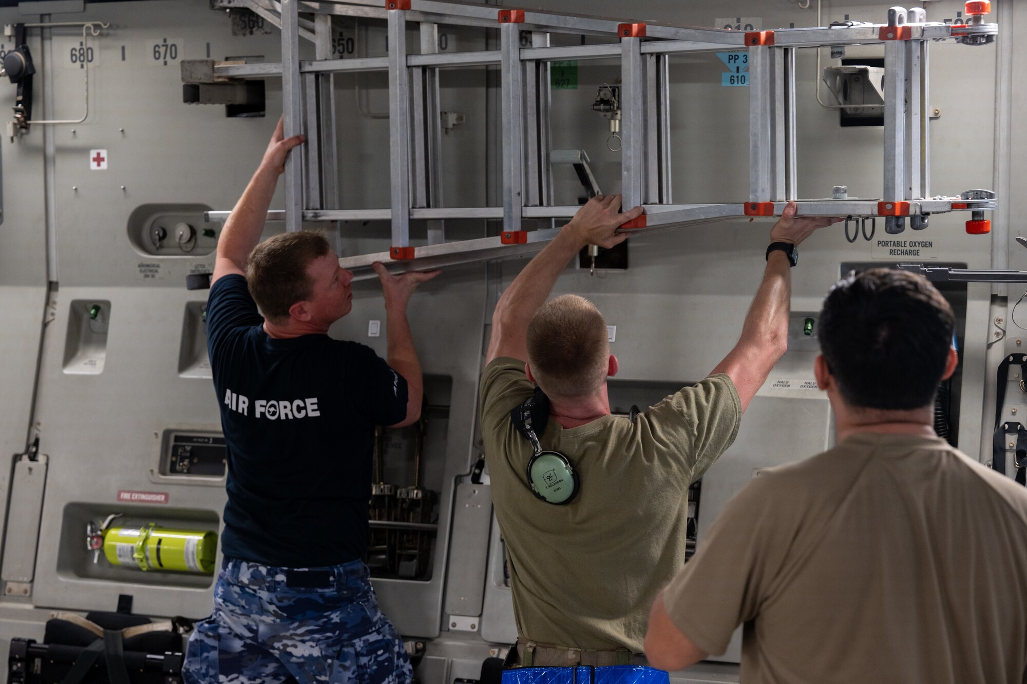 A U.S. Airman and a Royal Australian Air Force Airman work together to latch a ladder inside a C-17 Globemaster III.