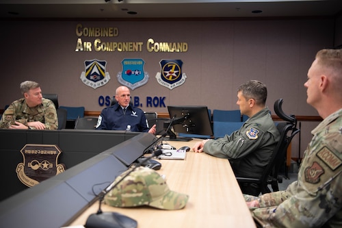 Chief Master Sgt. of the Air Force David Flosi sits at a table with Col. Tanner Woolsey,  607th Air Operations Center commander, and Chief Master Sgt. Jeremiah Ross, Seventh Air Force command chief, inside the 607th AOC at Osan Air Base, Republic of Korea. Flosi, wearing a blue uniform, speaks as the others listen.