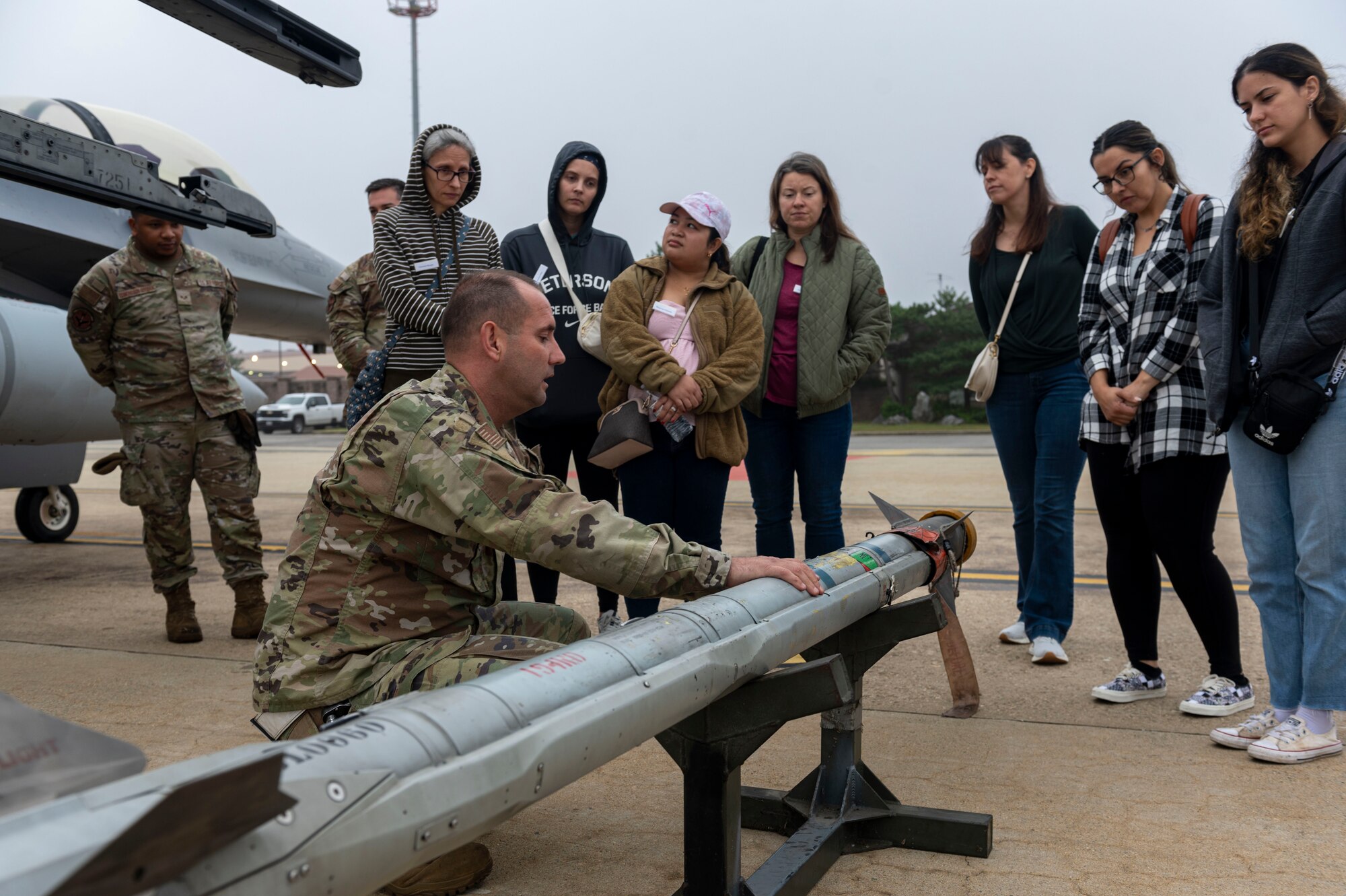 U.S. Air Force Tech. Sgt. Henry Winkler, 51st Maintenance Group loading standardization crew member, showcases how to load an air intercept missile during the Osan Spouse Immersion Tour at Osan Air Base, Republic of Korea, Oct. 16, 2024. During the tour, spouses were able to work closely with Airmen and learn how their daily operations directly contribute to the mission of the 51st Fighter Wing. (U.S. Air Force photo by Senior Airman Kaitlin Frazier)