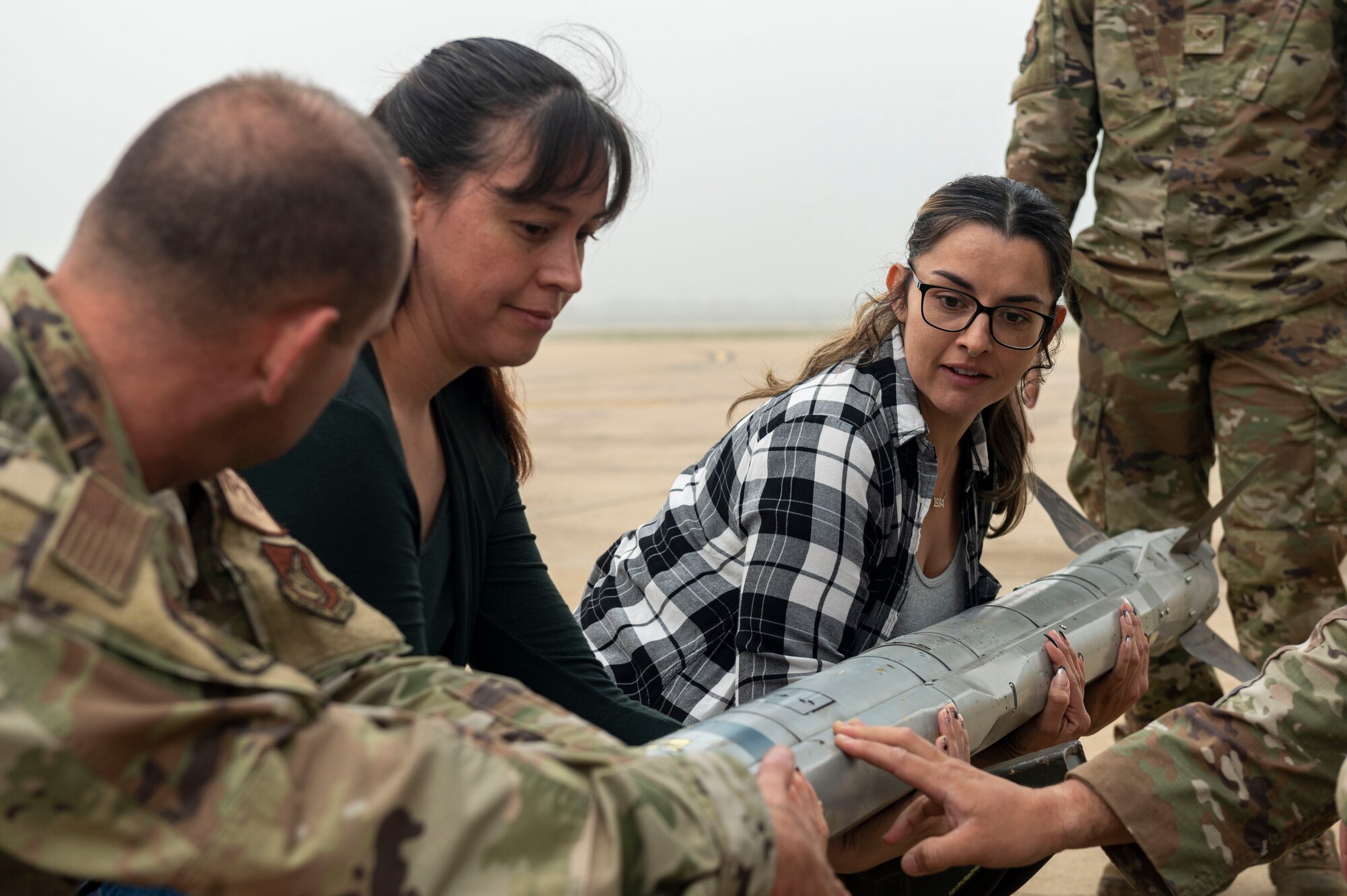 U.S. Air Force members assigned to the 51st Maintenance Group help Osan spouses lift an air intercept missile during the Osan Spouse Immersion Tour at Osan Air Base, Republic of Korea, Oct. 16, 2024. 51st MXG Airmen have provided the 51st FW with maintenance support for nearly 59 years during periods of war and peace. (U.S. Air Force photo by Senior Airman Kaitlin Frazier)