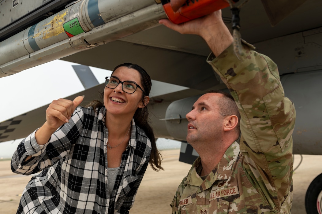 U.S. Air Force Tech. Sgt. Henry Winkler, 51st Maintenance Group loading standardization crew member, teaches Crystal Sanchez, Osan spouse, how to load an air intercept missile during the Osan Spouse Immersion Tour at Osan Air Base, Republic of Korea, Oct. 16, 2024. Airmen assigned to the 51st MXG have provided the 51st Fighter Wing with maintenance support for nearly 59 years during periods of war and peace. (U.S. Air Force photo by Senior Airman Kaitlin Frazier)