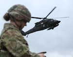 U.S. Army Spc. Jazmyne Wanger, a combat medic specialist with the Headquarters and Headquarters Company, 56th Stryker Brigade Combat Team, Pennsylvania National Guard, tends to a simulated wounded Soldier while an HH-60 Black Hawk helicopter draws near the pickup site during an air medevac exercise at Grafenwoehr Training Area Oct. 11, 2024.