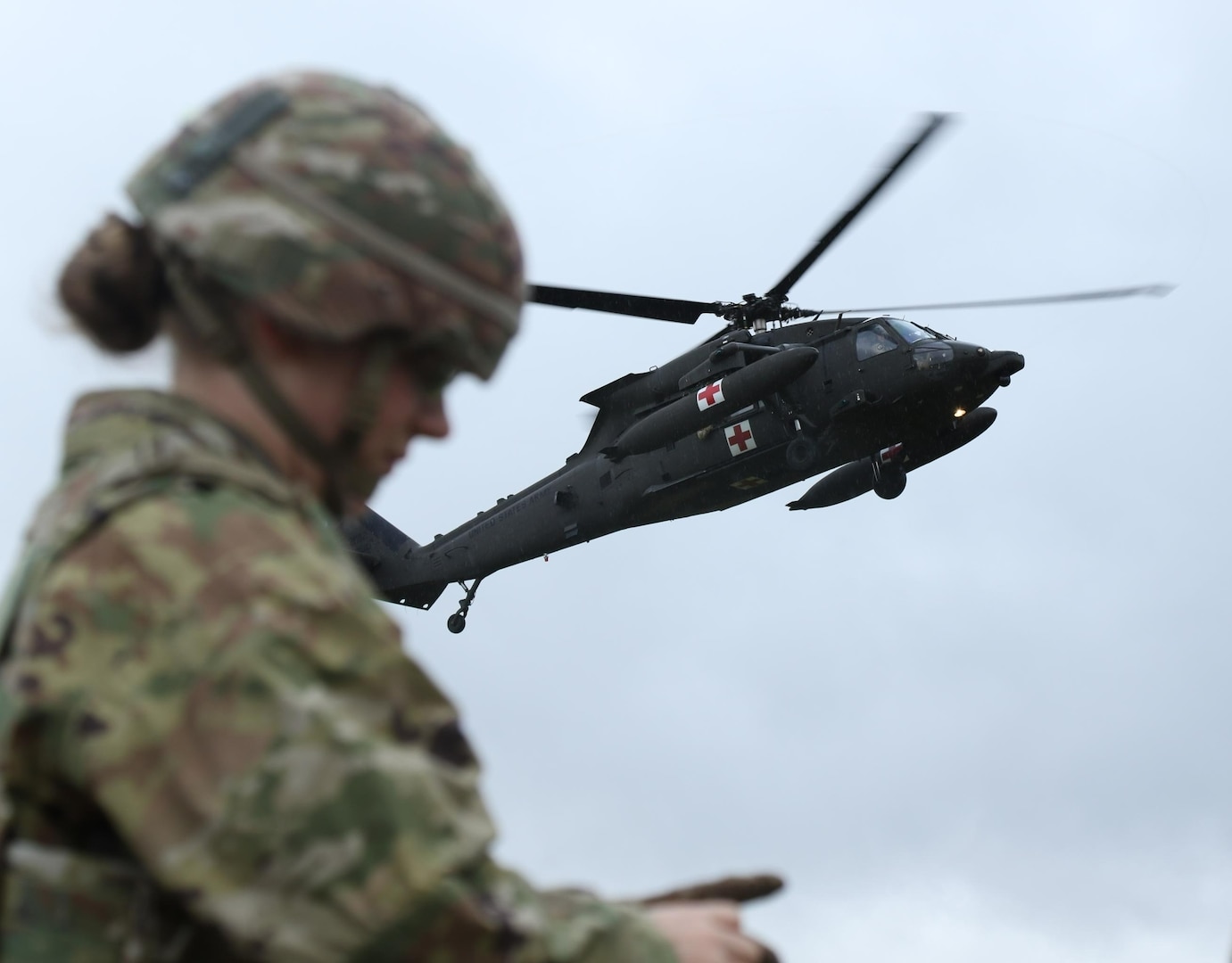 U.S. Army Spc. Jazmyne Wanger, a combat medic specialist with the Headquarters and Headquarters Company, 56th Stryker Brigade Combat Team, Pennsylvania National Guard, tends to a simulated wounded Soldier while an HH-60 Black Hawk helicopter draws near the pickup site during an air medevac exercise at Grafenwoehr Training Area Oct. 11, 2024.