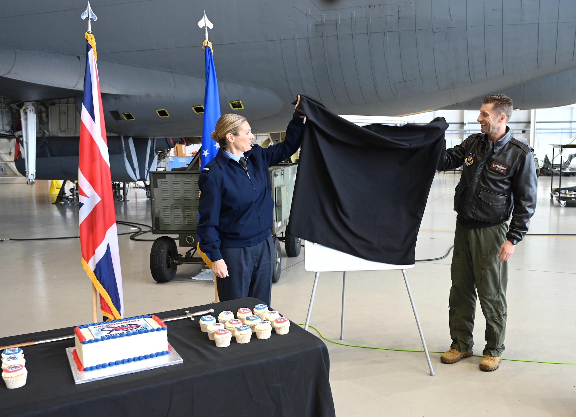 Royal Air Force Air Commodore Claire O’Grady, left, Deputy Air Officer Commanding No. 2 Group, and U.S. Air Force Col. Ryan Garlow, 100th Air Refueling Wing commander, prepare to unveil the new station crest – the Tudor Crown – at an event for Vice Lord-Lieutenants, Deputy Lieutenants, High Sheriffs, RAF representatives and other invited guests from the local community at RAF Mildenhall, England, Oct. 9, 2024. The Tudor Crown, used by HRH King Charles III, replaced the St. Edward’s Crown formerly used by HRH Queen Elizabeth II and will be placed on the tails of all 100th ARW KC-135 Stratotankers. The event also marked the 90th anniversary of RAF Mildenhall. (U.S. Air Force photo by Karen Abeyasekere)