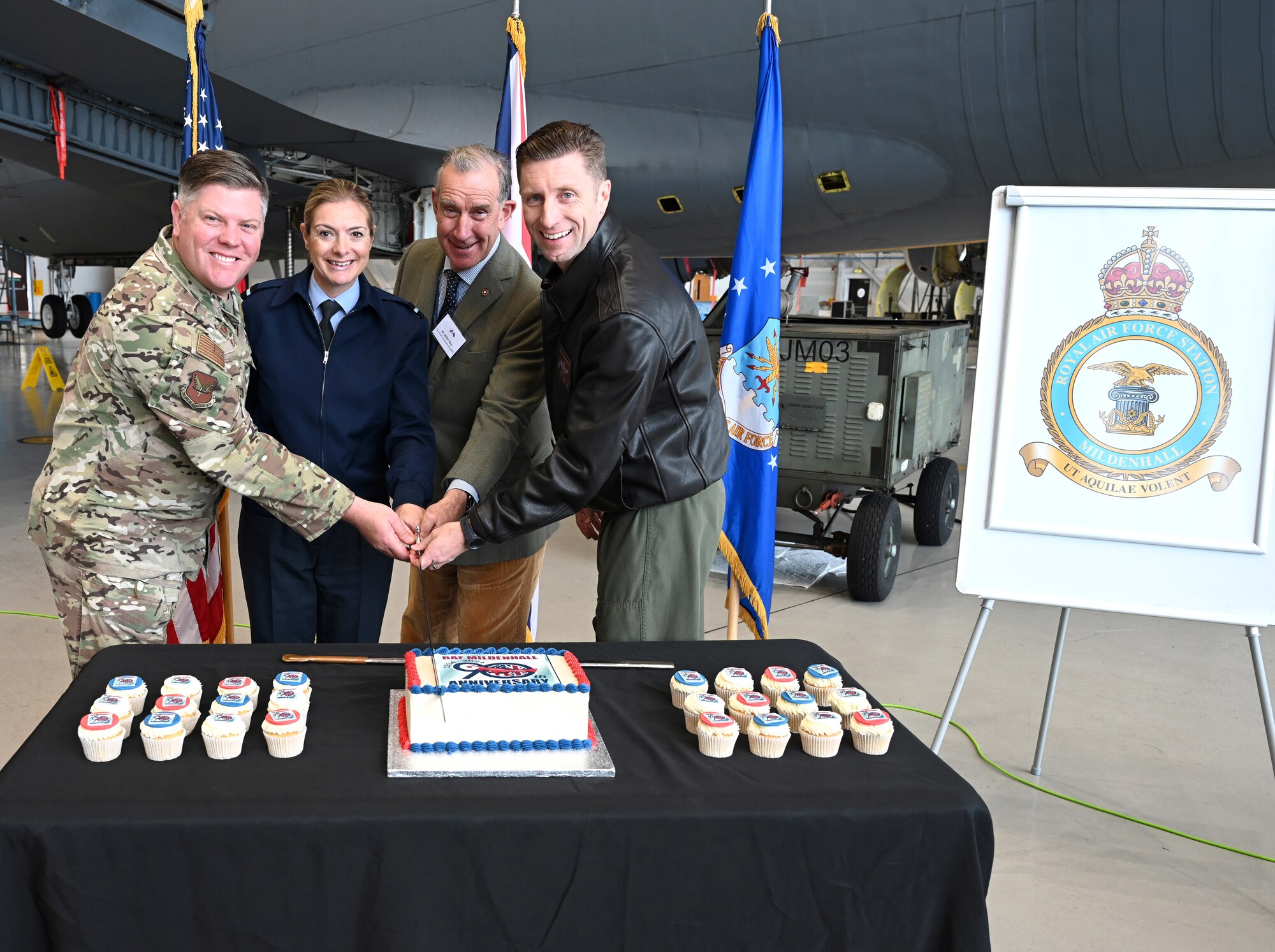 U.S. Air Force Col. Adam Moore, left, 352nd Special Operations Wing; Royal Air Force Air Commodore Claire O’Grady, second left, Deputy Air Officer Commanding No. 2 Group; Robert Rous, second right, Vice Lord-Lieutenant of Suffolk; and U.S. Air Force Col. Ryan Garlow, 100th Air Refueling Wing commander, use a sabre to cut a cake celebrating RAF Mildenhall’s 90th anniversary of being an RAF station during a special event Oct. 9, 2024. The celebration also included the unveiling of a new station crest – the Tudor Crown – at an event for Vice Lord-Lieutenants, Deputy Lieutenants, High Sheriffs, RAF representatives and other invited guests from the local community. The Tudor Crown, used by HRH King Charles III, replaced the St. Edward’s Crown formerly used by HRH Queen Elizabeth II and will be placed on the tails of all 100th ARW KC-135 Stratotankers. (U.S. Air Force photo by Karen Abeyasekere)