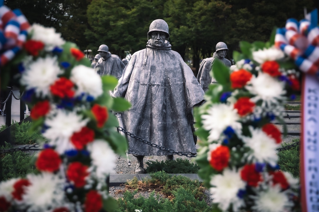 Statues are pictured with ceremonial wreaths in the foreground during daylight.