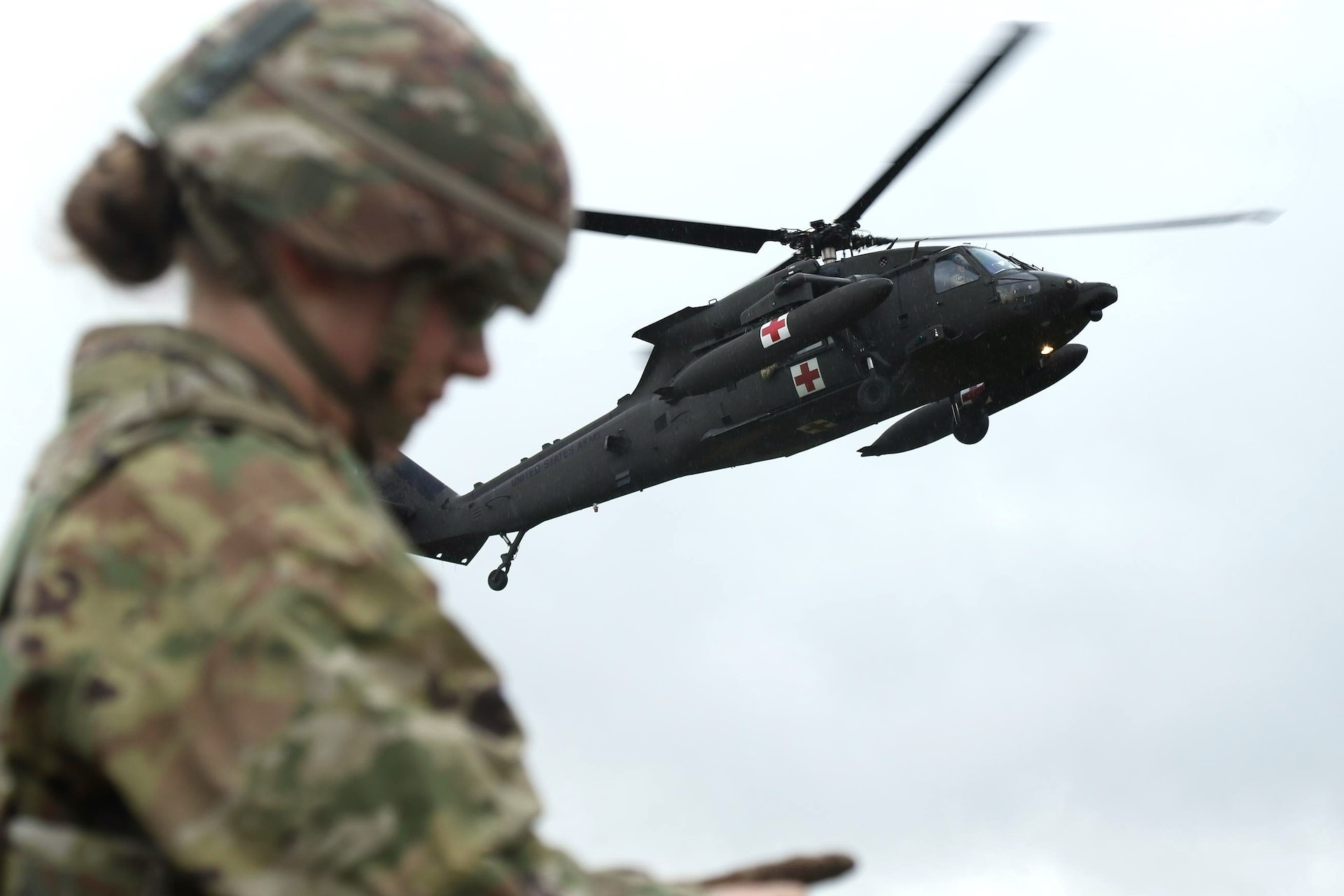 Spc. Jazmyne Wanger, a combat medic specialist with the Headquarters and Headquarters Company, 56th Stryker Brigade Combat Team, Pennsylvania National Guard, continues tending to a simulated wounded soldier while an HH-60 Black Hawk helicopter draws near the pickup site during an air medevac exercise at Grafenwoehr Training Area, Oct. 11, 2024. U.S. Army medics rehearse their evacuation procedures to stand ready to respond to real life medical emergencies. (U.S. Army National Guard photo by Capt. Leanne Demboski)