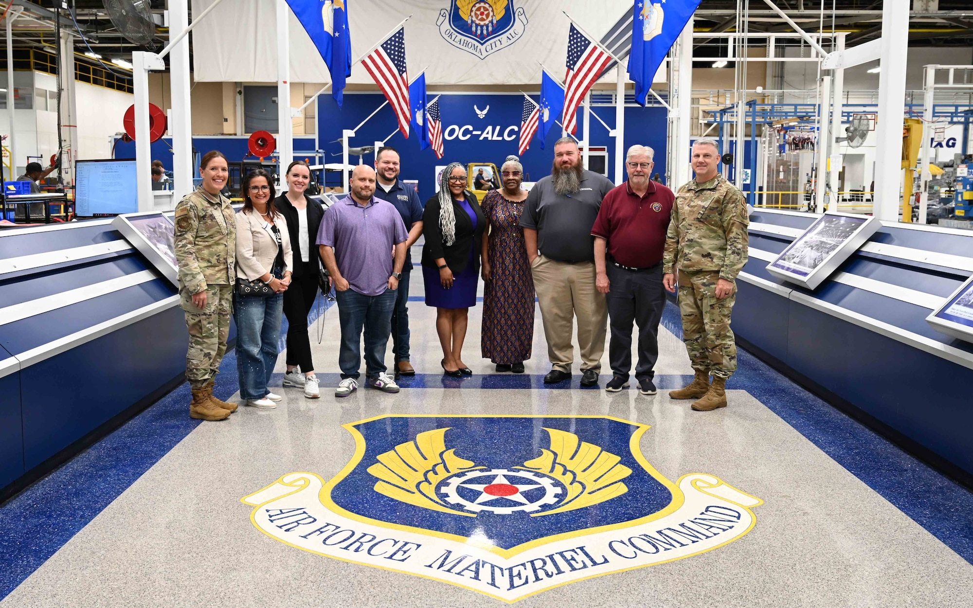 A group of people standing for a ceremonial photo behind a large emblem and hall of flags.