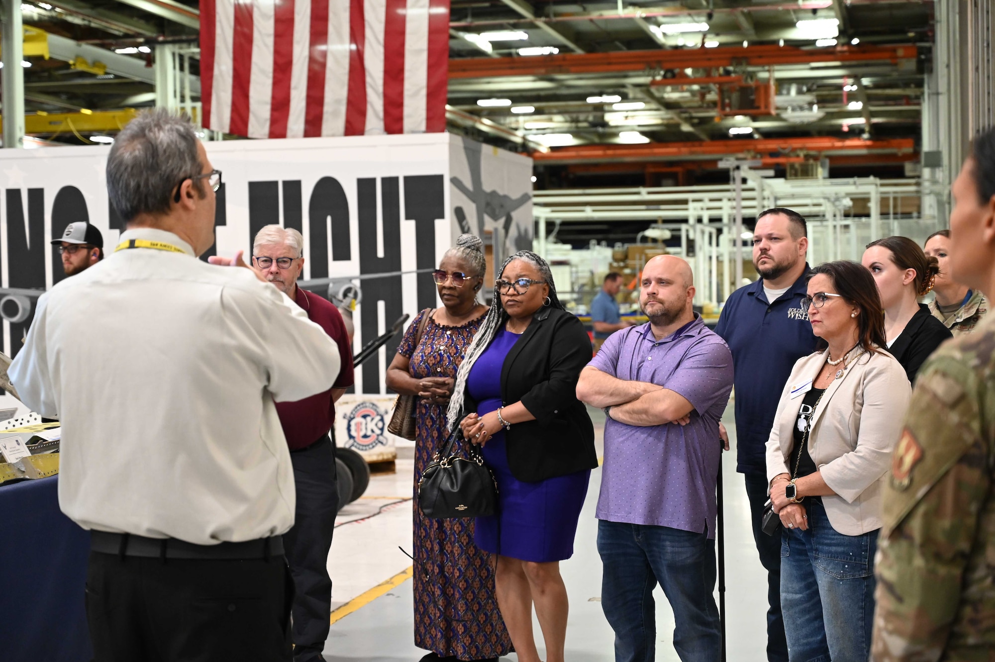 A group of people standing inside a large building listening to a presentation.