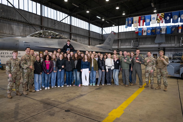 Students and base personnel stand in front of an F-16 Fighting Falcon.