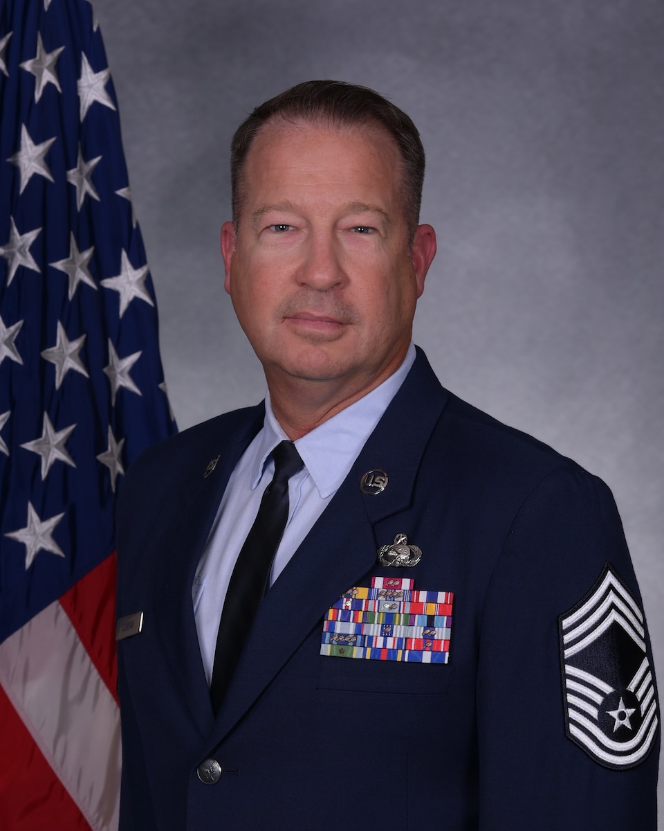 Man in dress blues posing for official photo in front of U.S. flag