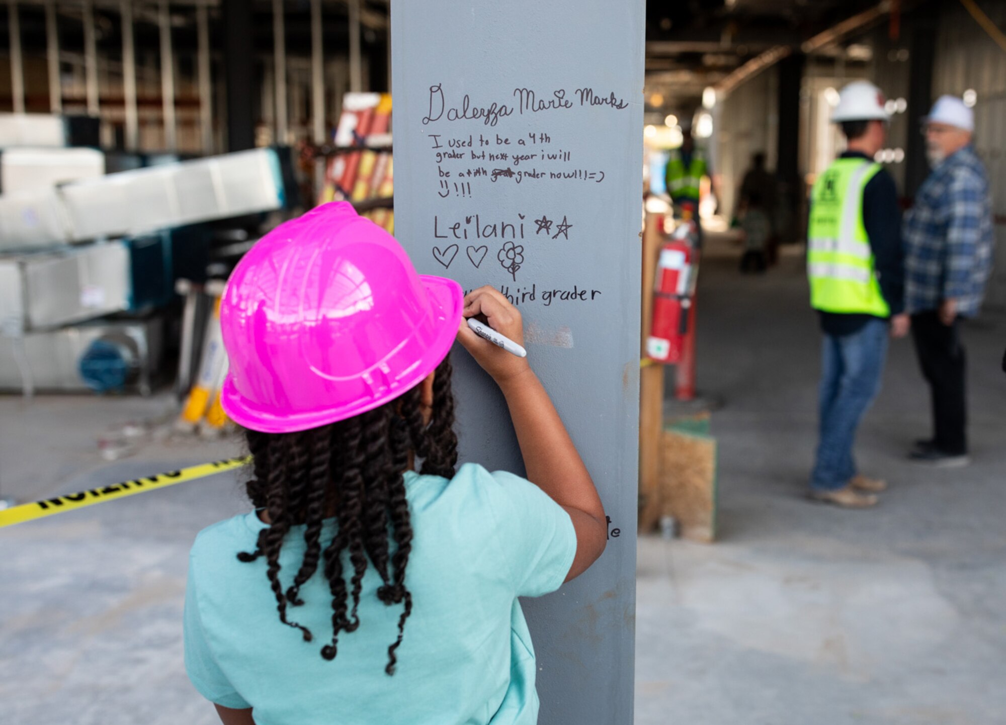 Student signs steel beam at construction site of new elementary school