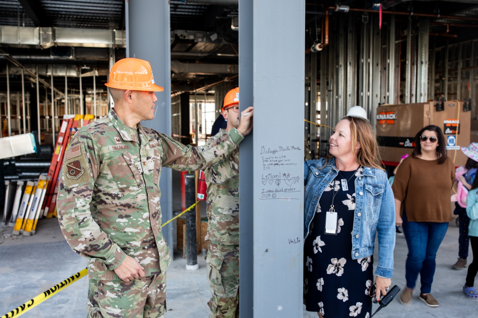 military man and civilian woman sign steel beam of newly constructed elementary school