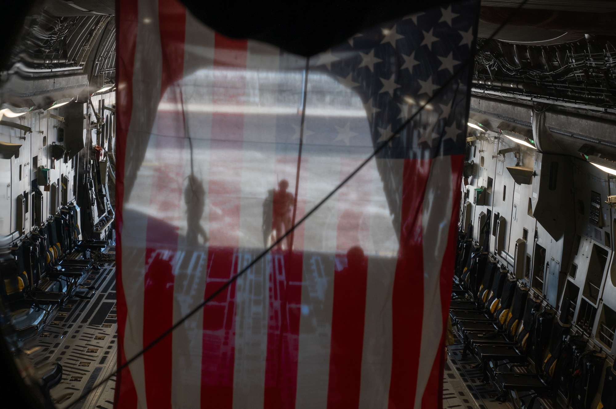 An American flag hangs inside a C-17 Globemaster III with the ramp open.
