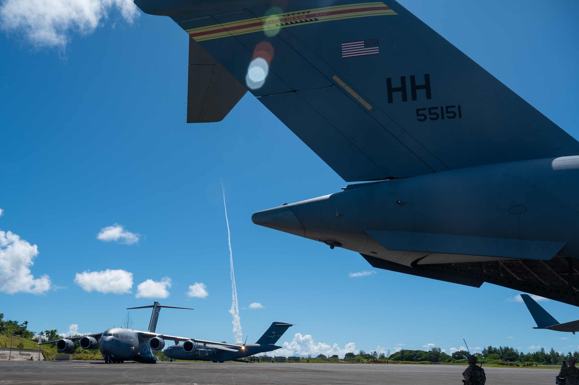 Three C-17 Globemaster IIIs parked an airfield in Palau while a missile is being launched in background.