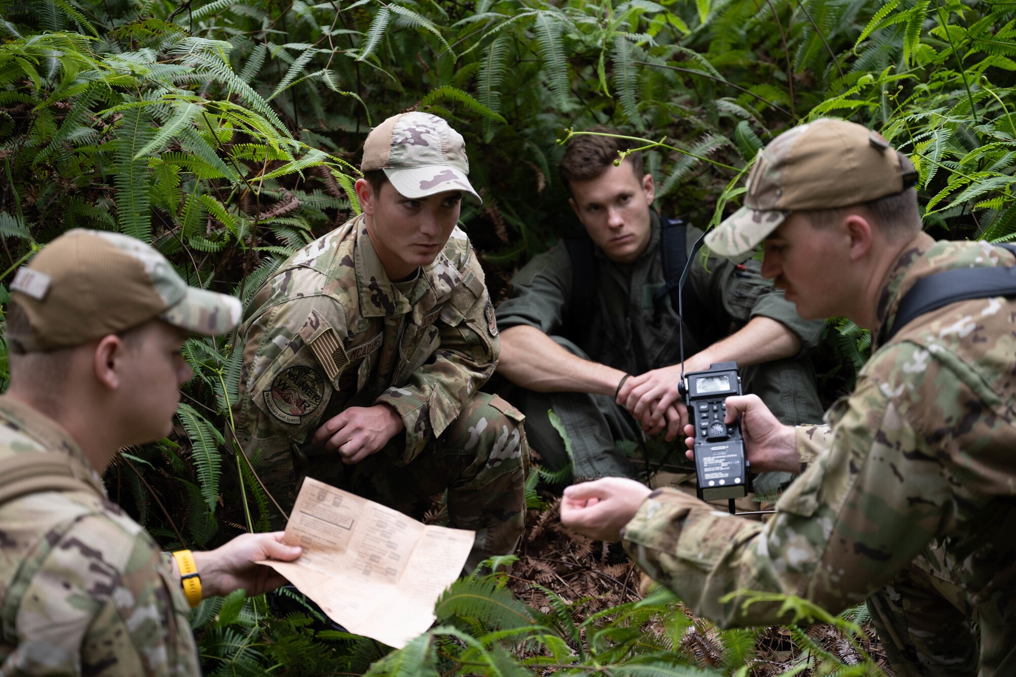 U.S. Air Force members sit in some greenery while looking at navigation equipment.
