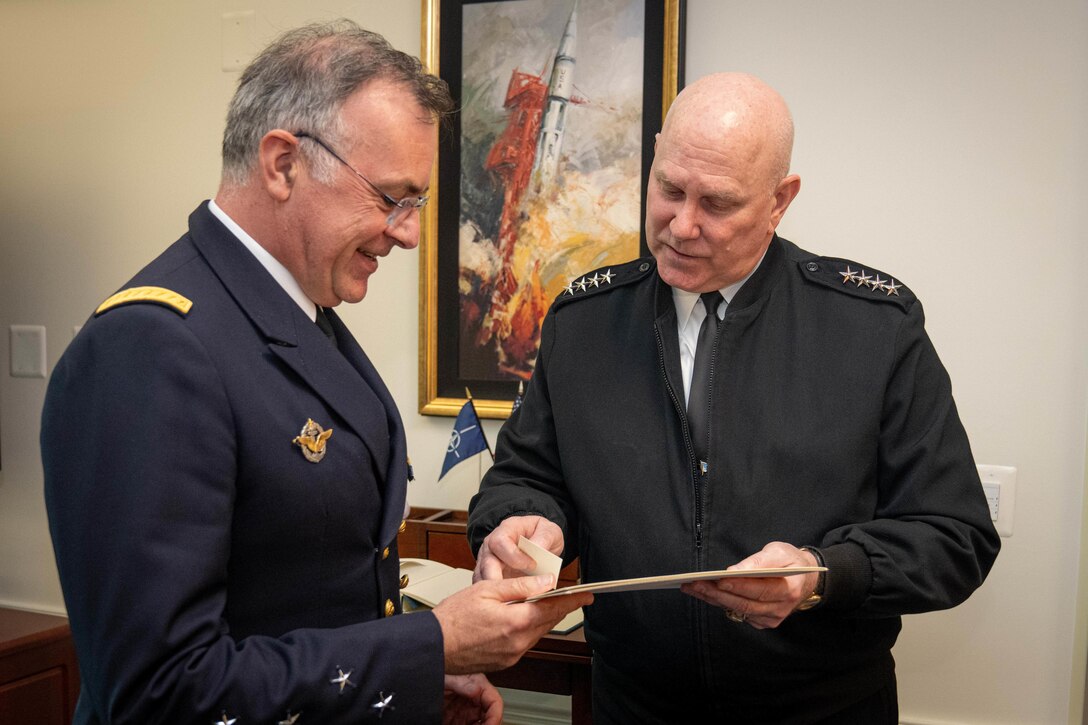 Two government officials look at a document in a room in front of a painting.