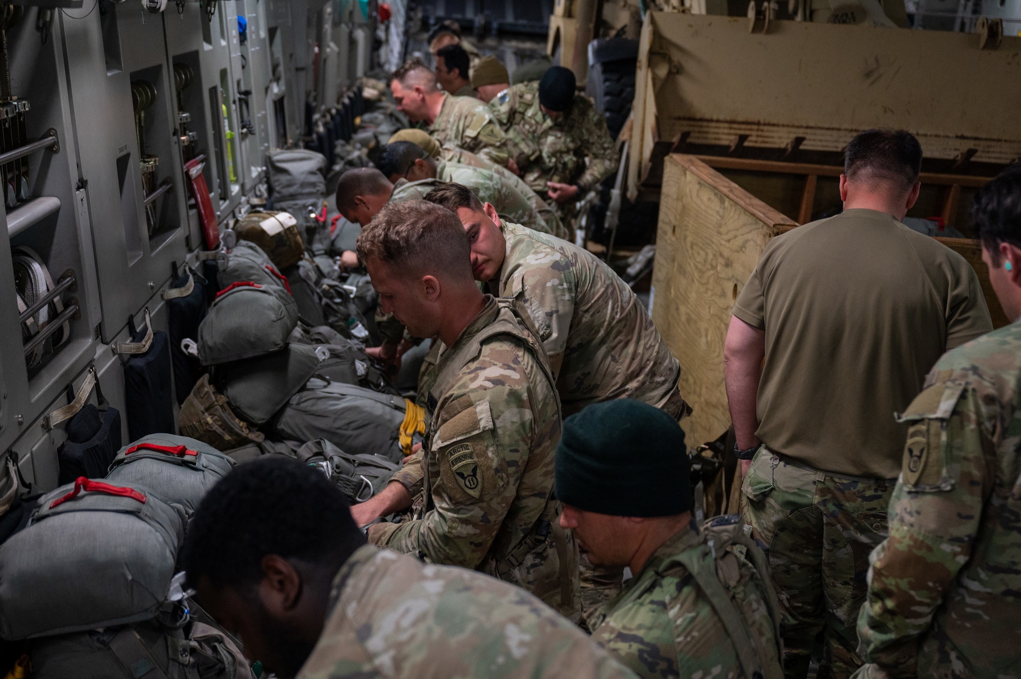 A group of Soldiers get up from their seats and prepare their parachutes.
