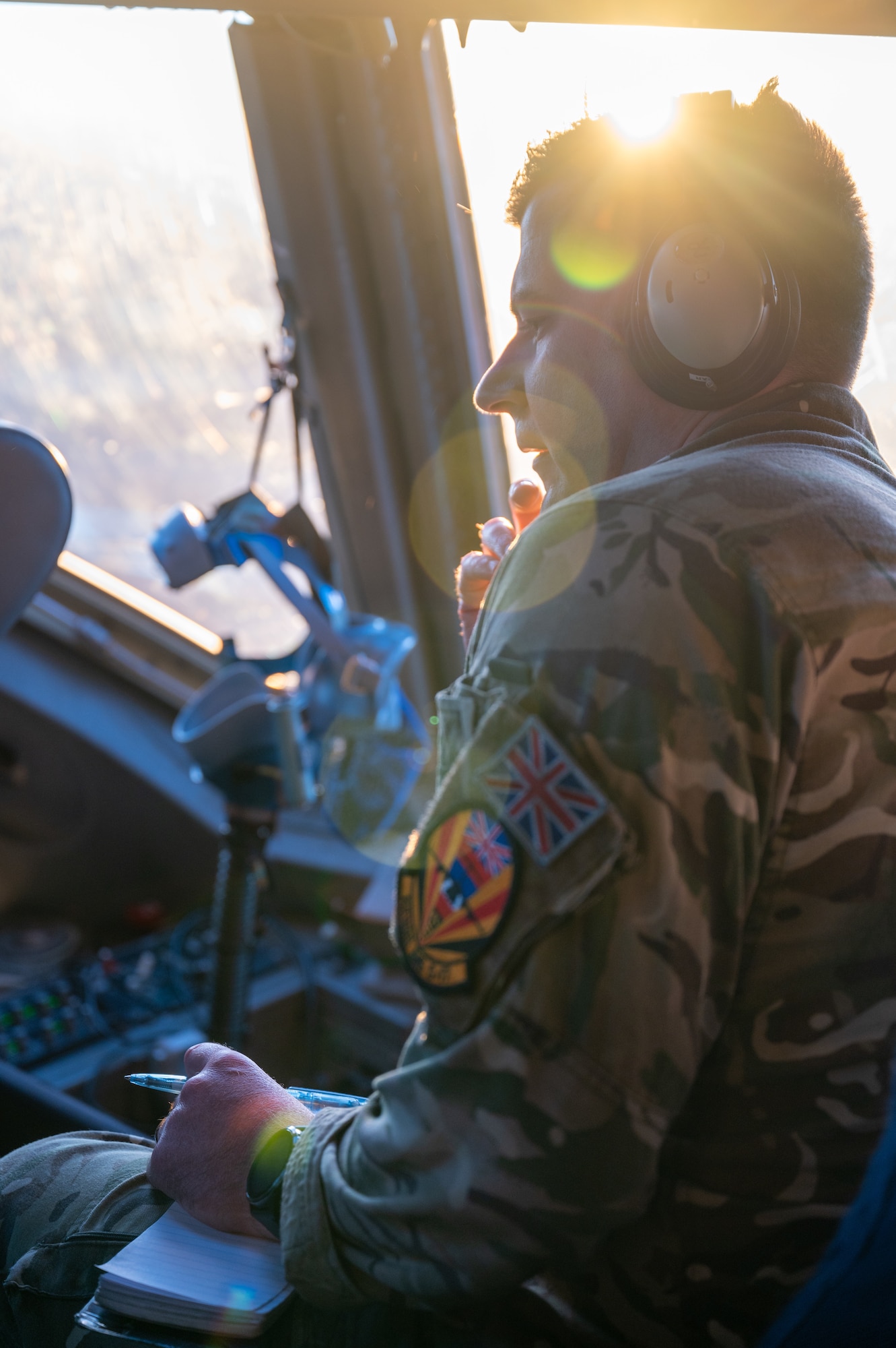 Royal Air Force member talks on a microphone headset while inside a flying C-17 Globemaster III aircraft.