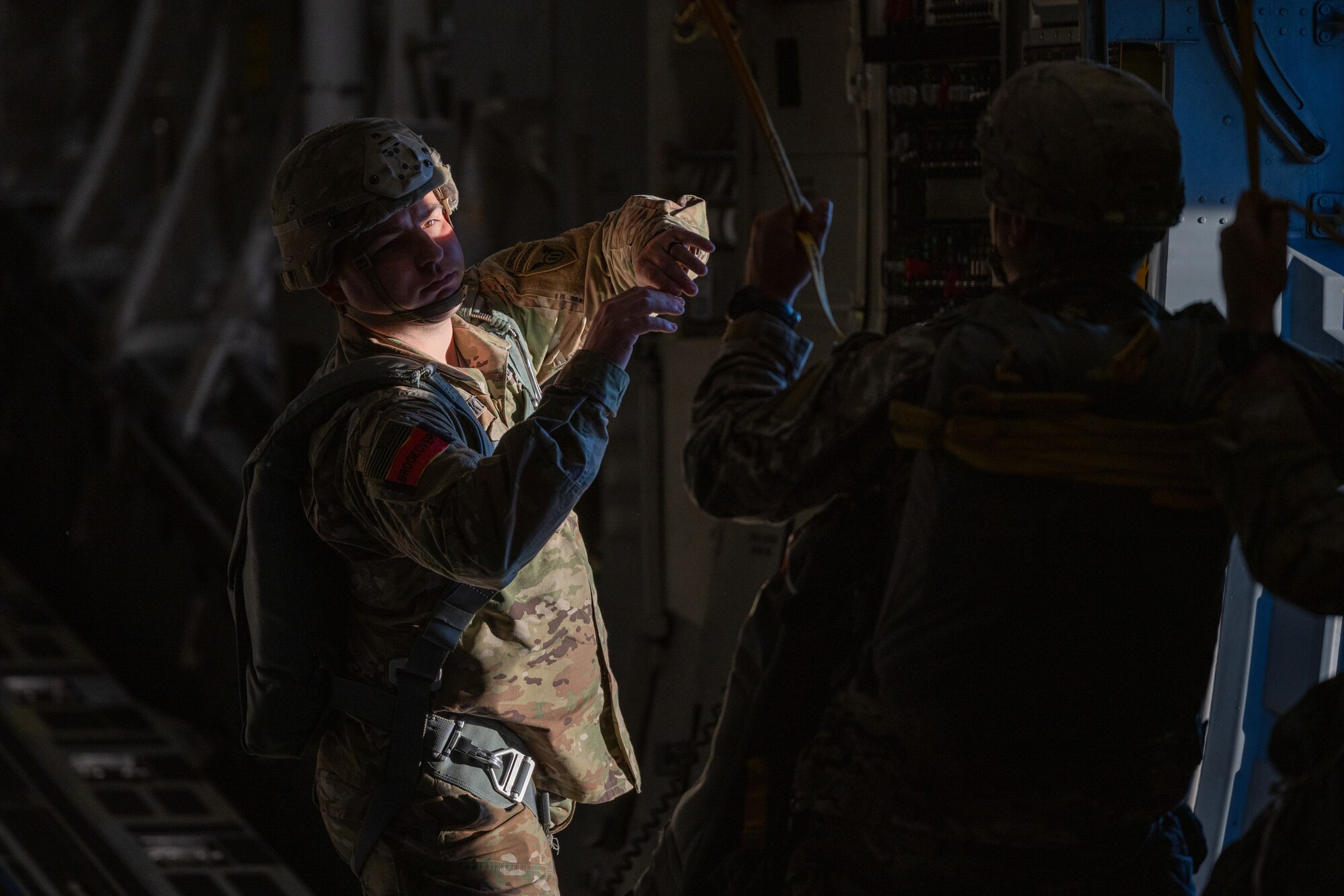 A U.S. Army Soldier stands by the exit of a flying C-17 Globemaster III aircraft guiding a fellow soldier parachuting out.