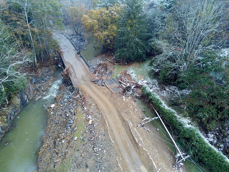a damaged bridge rests partially in a creek bed.