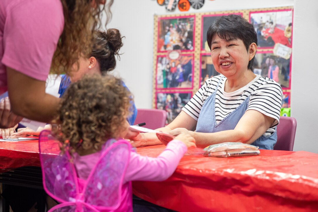 Noriko Narusaka, a volunteer with the Marine Corps Air Station Iwakuni Japanese American Society, right, writes a child's name in Japanese during a fall festival hosted by the MCAS Iwakuni American Red Cross, Navy Marine Corps Relief Society, Japanese American Society, Fire and Emergency Services, the food pantry, and the Exceptional Family Members Program at the community support center at MCAS Iwakuni, Japan, Oct. 10, 2024. The fall festival is an event open to all base personnel and offers the opportunity to take part in fall festivities while learning about programs offered at the community support center. (U.S. Marine Corps Photo by Sgt. Calah Thompson)