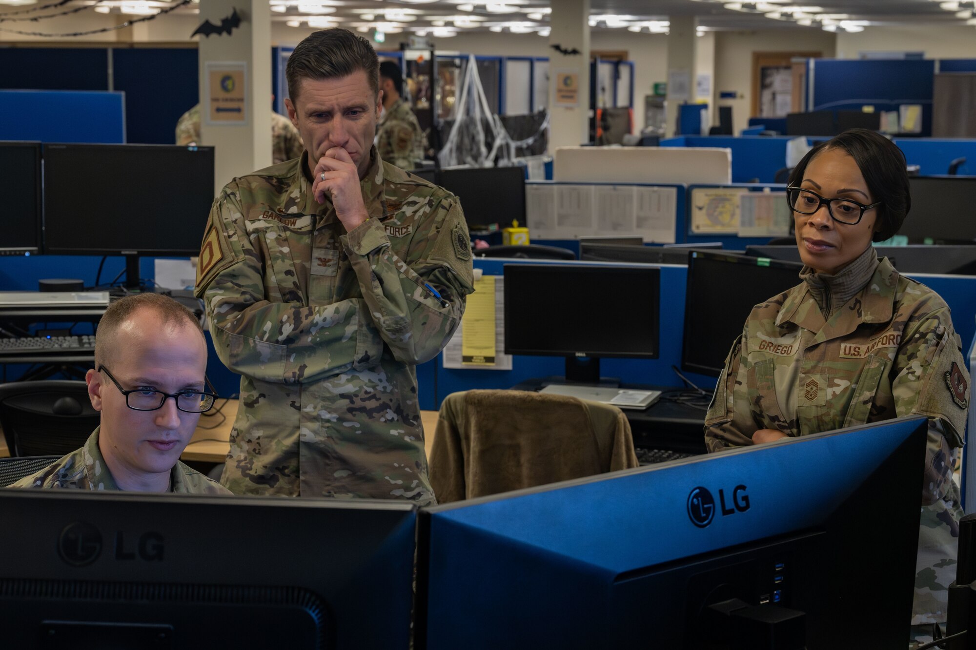 U.S. Air Force Airman 1st Class Andrew Simons, left, 100th Communications Squadron client systems technician, Col. Ryan Garlow, center, 100th Air Refueling Wing commander, and Chief Master Sgt. Tiffany Griego, 100th ARW command chief, look at a database of all computers assigned to the installation during a “Day in the Life” integration with the 100th CS at Royal Air Force Mildenhall, England, Oct. 18, 2024.