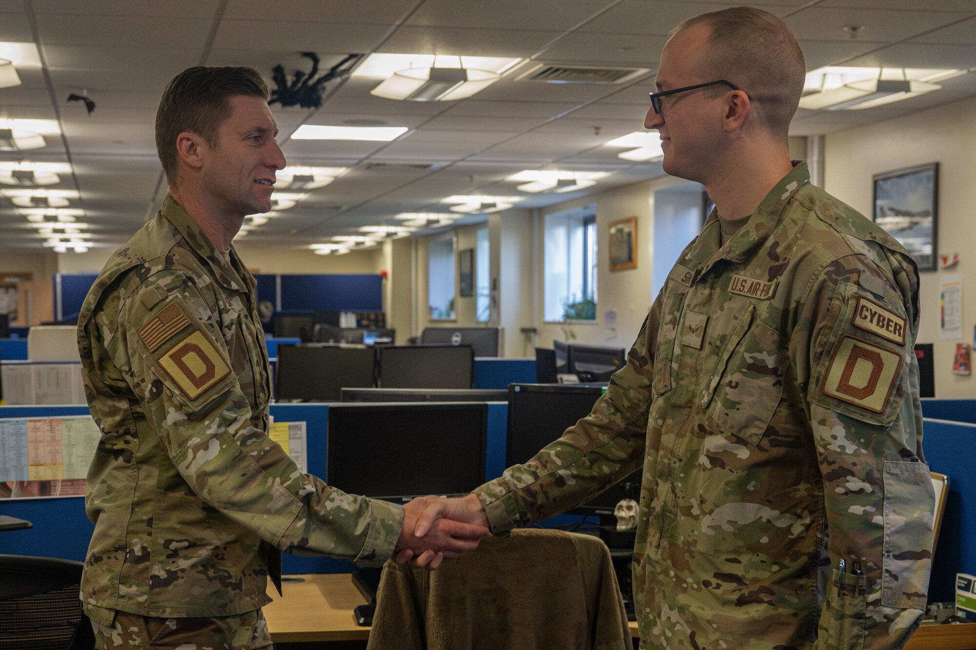 U.S. Air Force Airman 1st Class Andrew Simons, right, 100th Communications Squadron client systems technician, receives a coin from Col. Ryan Garlow, 100th Air Refueling Wing commander, during a “Day in the Life” integration with the 100th CS at Royal Air Force Mildenhall, England, Oct. 18, 2024.