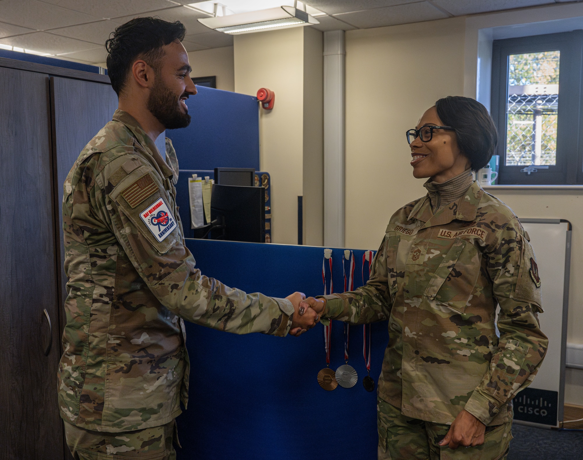 U.S. Air Force Airman 1st Class Hashmat Alikozay, left, 100th Communications Squadron network system technician, receives a coin from Chief Master Sgt. Tiffany Griego, 100th Air Refueling Wing command chief, during a “Day in the Life” integration with the 100th CS at Royal Air Force Mildenhall, England, Oct. 18, 2024.