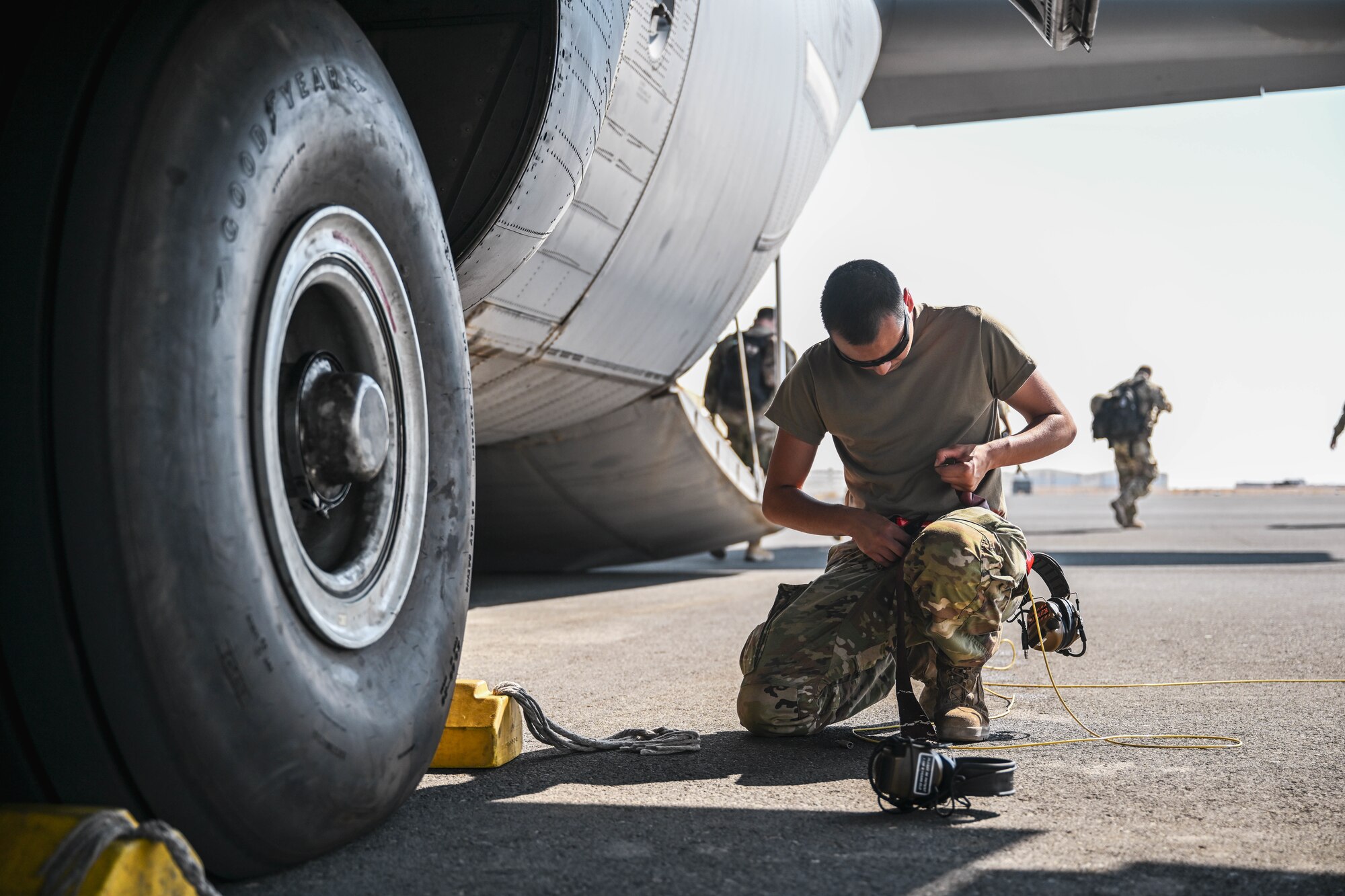 A uniformed service member inspects an aircraft tire on the flightline.