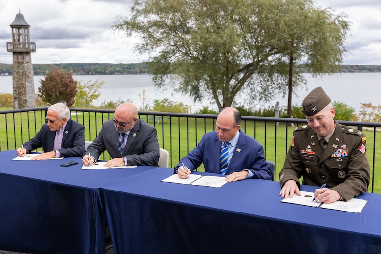 Four men seated at a table signing documents.