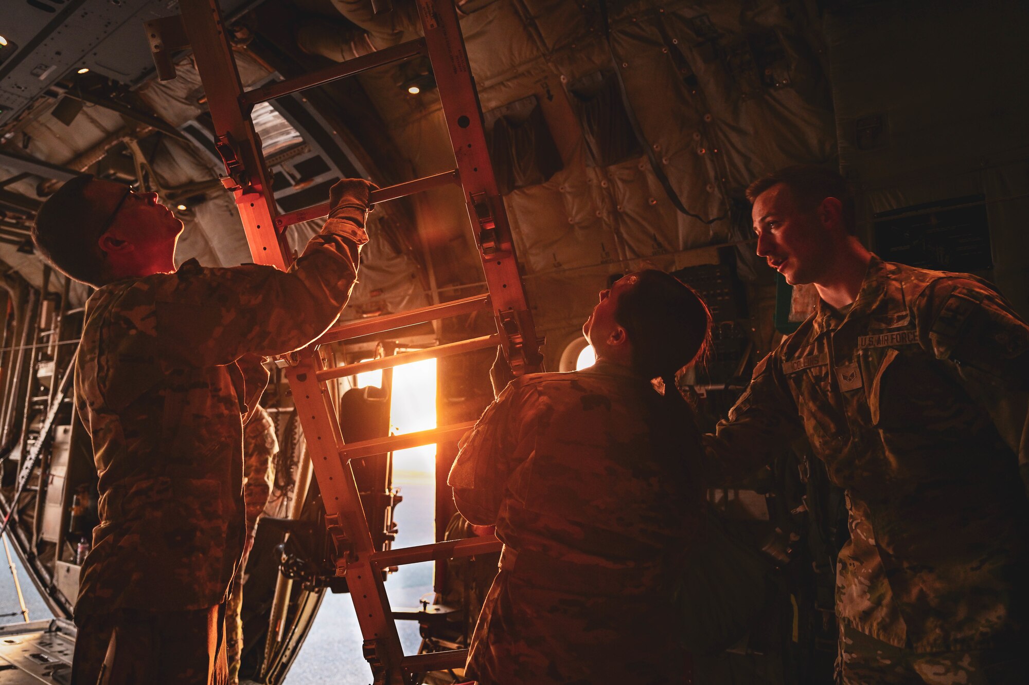 A man holds a ladder while two others watch him.