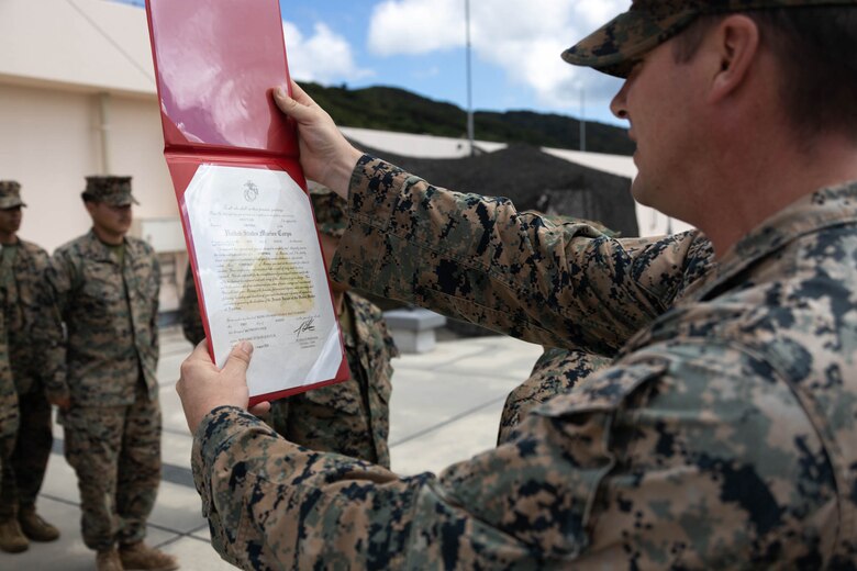 U.S. Marine Corps Staff Sgt. Jack Kemppainen, a transmissions chief with 12th Marine Littoral Regiment, 3d Marine Division reads a promotion warrant while conducting a promotion ceremony during exercise Resolute Dragon 24 at Japan Ground Self-Defense Force Camp Ishigaki, Okinawa, Japan, Aug. 1, 2024. Cpl. Lee is the first Marine to be promoted into the noncommissioned officer ranks on JGSDF Camp Ishigaki. Lee’s responsibilities as a corporal in his military occupational specialty range from ensuring the technical and tactical proficiency of his subordinates to the management of more than $600,000 worth of communications gear. RD 24 is an annual bilateral exercise in Japan that strengthens the command, control, and multi-domain maneuver capabilities of U.S. Marines in III Marine Expeditionary Force and Japan Self-Defense Force personnel, with a focus on controlling and defending key maritime terrain. Kemppainen is a native of Montana. Lee is a native of Alaska.