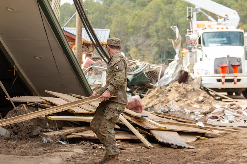 A soldier clears wooden debris from a pile.