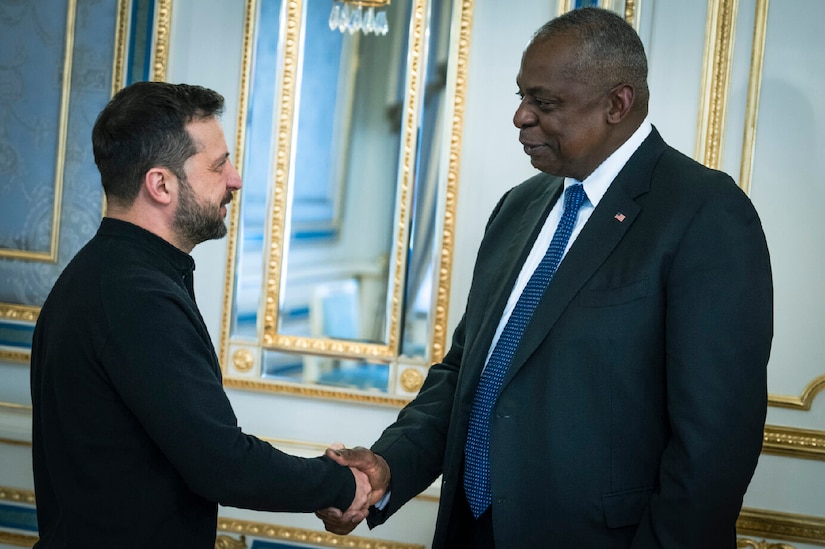 Two people in civilian attire shake hands in front of a mirrored wall.