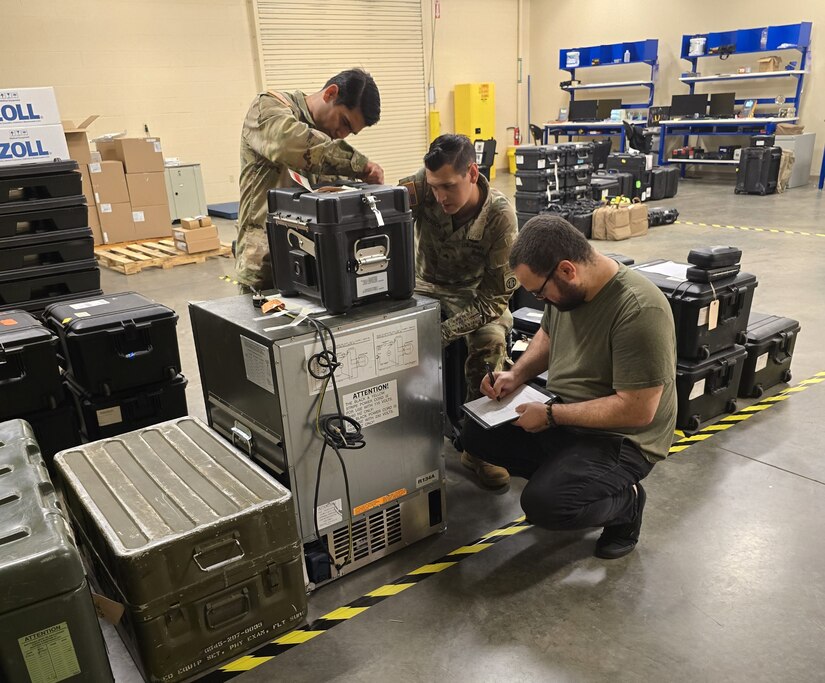 Three people are next to a line of medical equipment, inventorying.