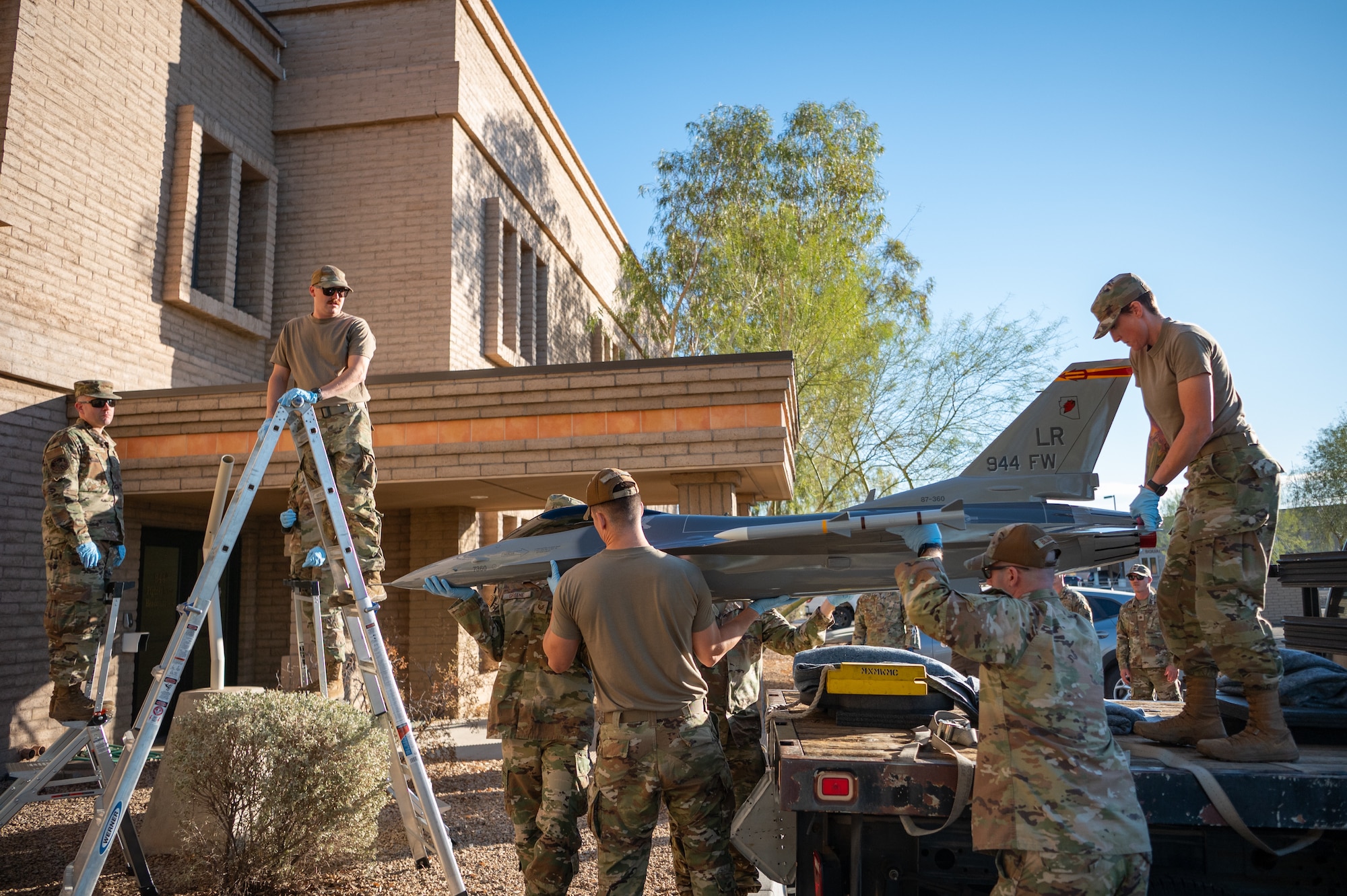 944th Fighter Wing members carefully maneuver a restored F-16 static display into position outside wing headquarters at Luke Air Force Base, Ariz., Oct. 17, 2024. The F-16, a nearly quarter-scale replica, honors the legacy of the wing and represents the teamwork and dedication of its personnel. (U.S. Air Force photo by Tech. Sgt. Tyler J. Bolken)