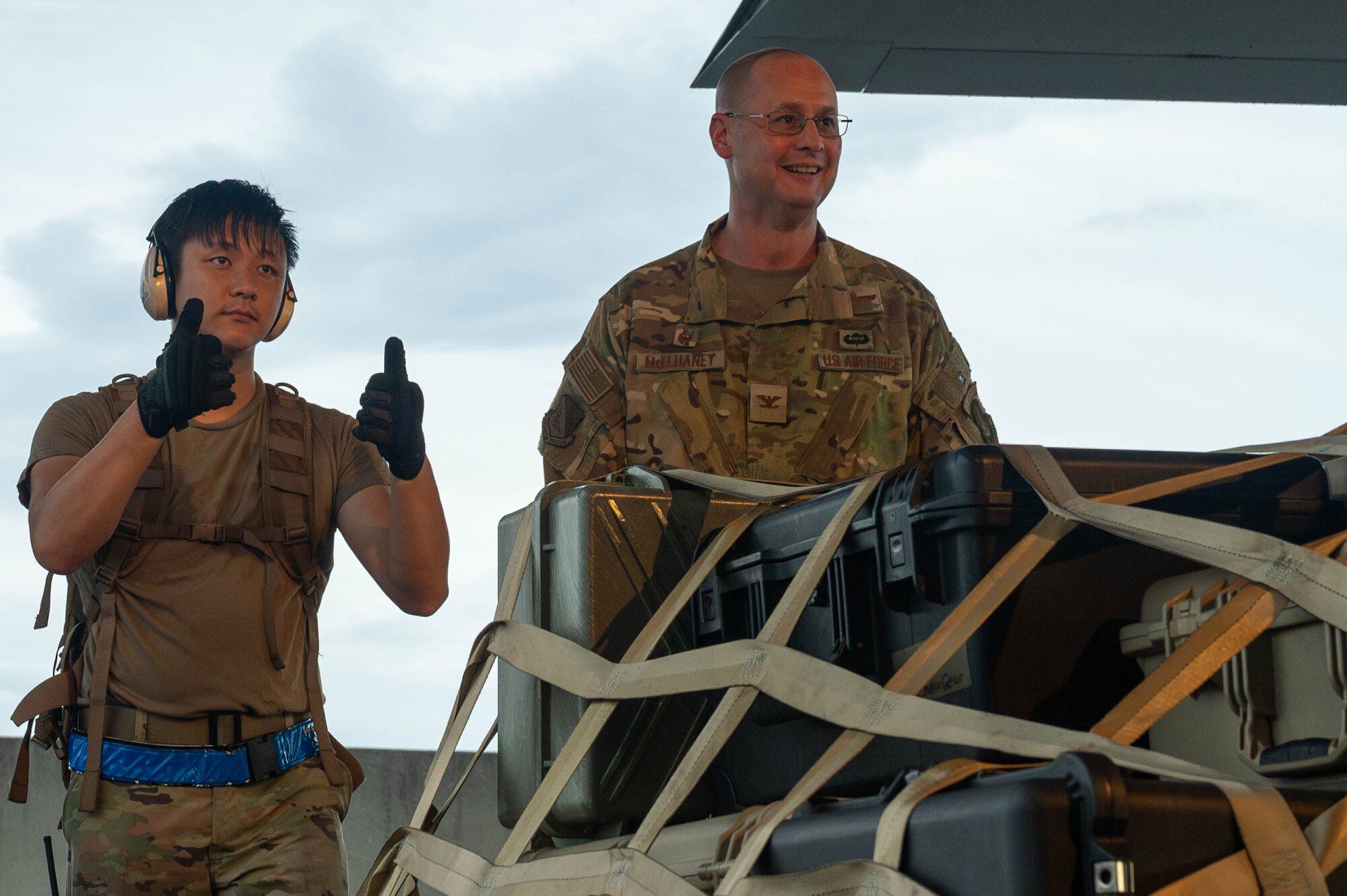 Two military members stand behind cargo.