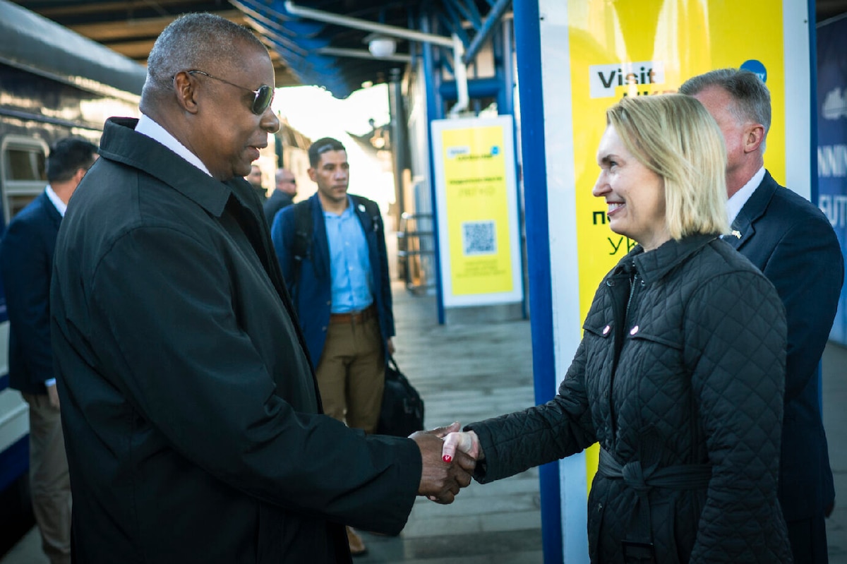 Two people shake hands and smile as others watch.
