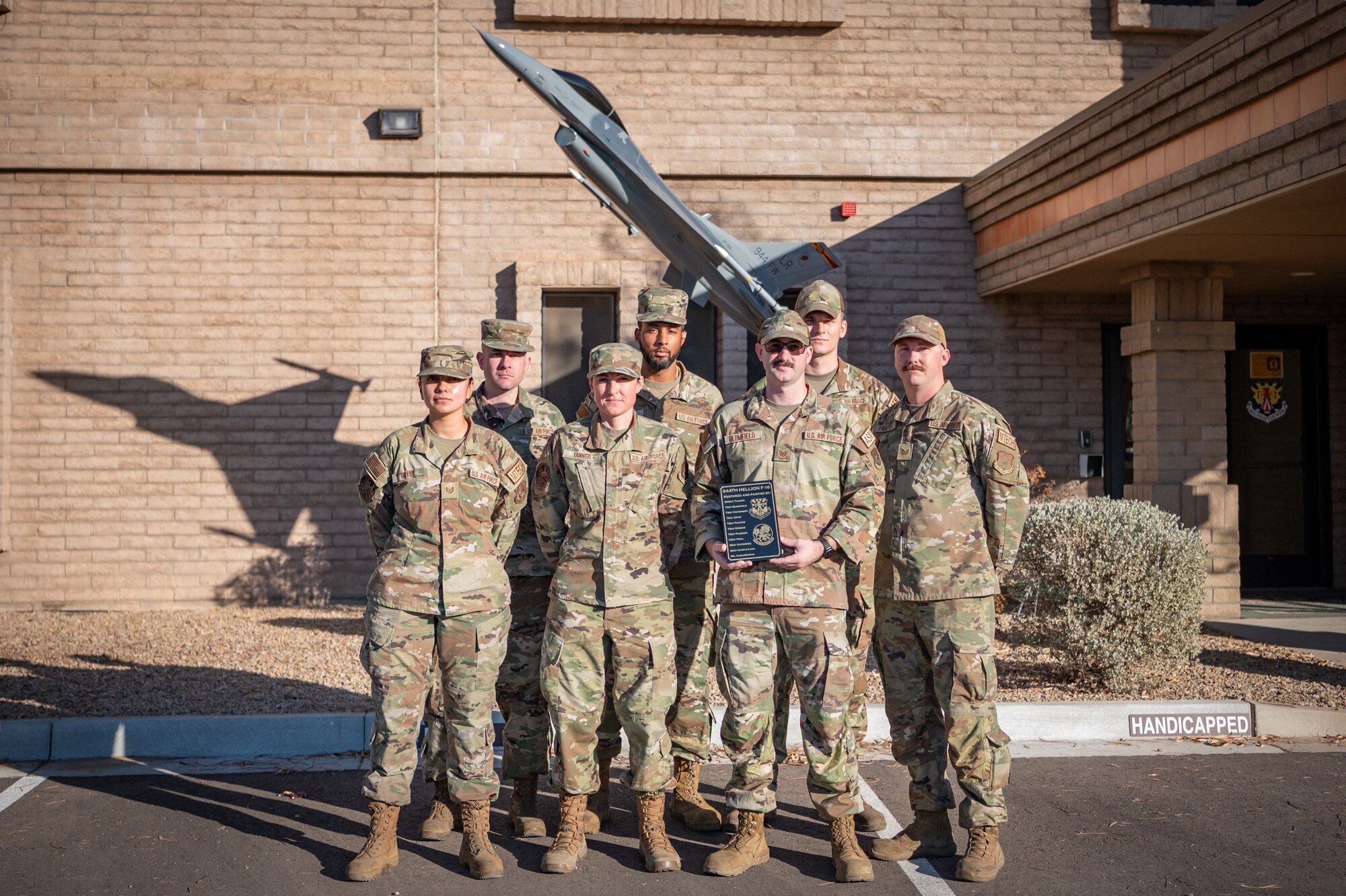 A group of 944th Fighter Wing maintainers pose in front of the newly restored F-16 static display outside wing headquarters at Luke Air Force Base, Ariz., Oct. 17, 2024. The team's craftsmanship and attention to detail were central to the restoration, which honors both the past and future of the wing. (U.S. Air Force photo by Tech. Sgt. Tyler J. Bolken)